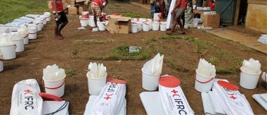des kits EHA, blanc à l'effigie de la croix rouge (seaux et ustensiles en plastiques) alignés sur le sol rouge.