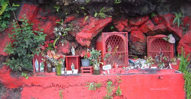 Chapelles de Saint Expédit en bord de route avec de nombreuses offrandes déposées devant, statuettes et fleurs. Tout le rocher autour est peint en rouge, couleur de Saint Expedit.
