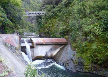 barrage sur rivière dans une vallée encaissée. Le dessus du barrage est recouvert d'une dalle avec goute de pluie comportant une ouverture où l'eau s'écoule