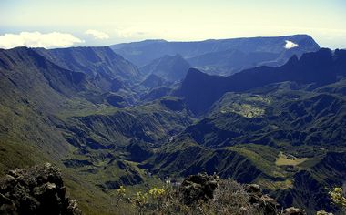 Vue en plongée sur le cirque de Mafate, vaste étendue montagneuse, verdoyante et accidentée entourée d'une caldeira ouverte au fond à gauche.