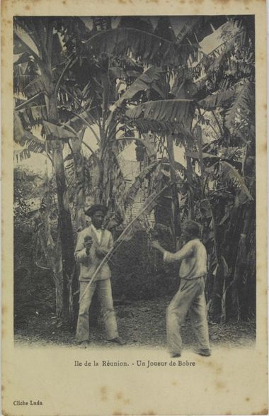 Carte postale ancienne avec un joueur de bobre et un danseur sous des bananiers. Légende: Île de la Réunion: joueur de bobre