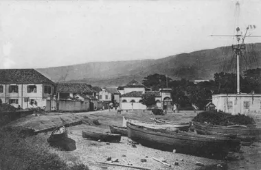 photo noir et blanc d'une petite lagune avec des barques avec un mât de signauxsur le coté droit et des bâtiments à l'arrière plan