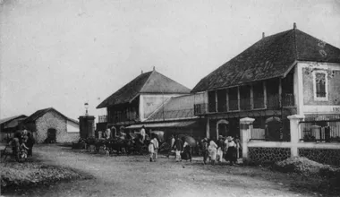 photo noir et blanc deux bâtiments au large toit reliés parun hall avec plusieurs personnes et des carrosses garés devant