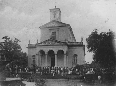 photo noir et blanc d'une grande église coloniale avec une façade formée de 2 arches et de nombreux fidèles sur le parvis