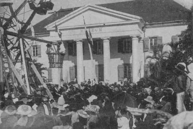 photo noir et blanc d'une foule devant une façade néoclassique blanche. Une grande roue en bois se tient sur le coté gauche