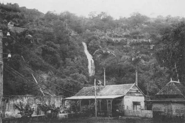 photo noir et blanc d'un bâtiment au pied d'une cascade d'où partent des fils électriques sur des poteaux