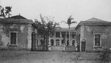 photo noir et blanc de l'entrée d'une caserne dont la grille est gardée par deux fantassins coloniaux.