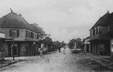 photo noir et blanc d'une rue bordée de grandes maisons aux façades de bois. Le fondde la rue est boisé