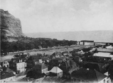 photo noir et blanc d'une rivière qui se jette dans la mer avec une falaise rive gauche et de nombreuses maisons rive droite